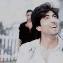 a man in a white shirt is smiling with a woman in a black jacket in the background