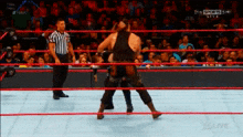 two wrestlers are fighting in a ring with a referee in the background