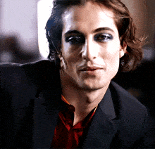 a close up of a man 's face with a red shirt and a black jacket