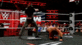 two men are wrestling in a wrestling ring with a w logo on the wall behind them