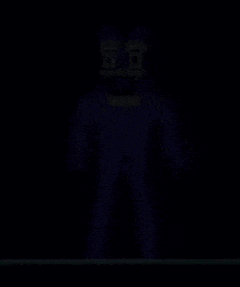 a blue cartoon character with yellow eyes and a yellow bow tie is standing in the dark .