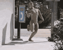 a naked man is running on a sidewalk in front of a payphone .