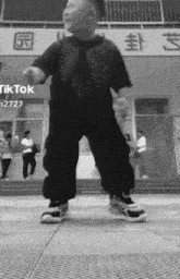 a black and white photo of a child dancing in front of a building with chinese writing on it .