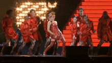 a woman in a red dress is dancing on a stage with other dancers