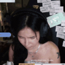 a woman wearing headphones is sitting in front of a wall with post it notes on it