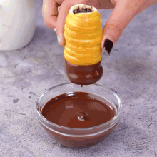 a person dipping a pastry in a bowl of chocolate