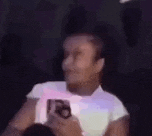 a woman in a white shirt is holding a cell phone in her hand .