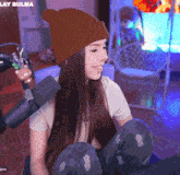a woman wearing a brown beanie is sitting in front of a microphone with the words lay bulma on the bottom right