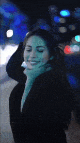 a woman wearing a black coat and a green sweater smiles