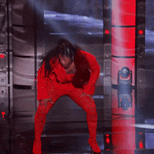 a woman in a red outfit is dancing in front of a red pillar