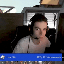 a man wearing headphones sits in front of a screen that says " live 24h "