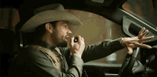 a man in a cowboy hat is talking on a walkie talkie in a car