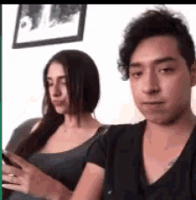 a man and a woman are sitting next to each other on a couch looking at their phones .