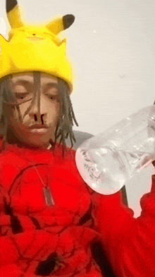 a man wearing a pikachu hat and a red sweater is holding a plastic bottle of water .