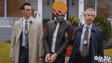 a man wearing a mask is being arrested by two police officers in front of a house with the number 351 on it