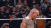 a man with a tattoo on his arm is standing in a wrestling ring with a crowd watching .