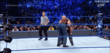 a wrestler is carrying another wrestler in a wrestling ring while a referee watches .