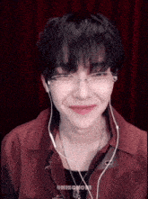 a young man wearing glasses and earbuds is smiling .