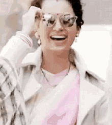 a woman wearing sunglasses and a pink scarf is smiling and laughing .