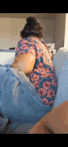 a woman in a floral shirt is sitting on a couch with her legs crossed .