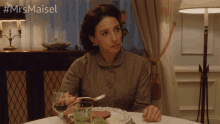 a woman sits at a table with a plate of food and a glass of wine with the hashtag #mrs maisel on the top
