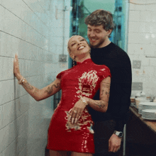a woman in a red dress is standing next to a man in a kitchen