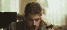 a man with a beard is sitting at a table with his hand on his head .