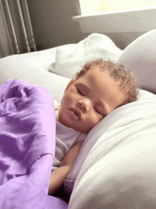 a baby is sleeping on a bed with a purple comforter