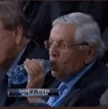 a man in a suit is drinking water from a bottle while sitting in a stadium