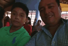 a man in a plaid shirt is taking a picture of a boy in a green polo shirt