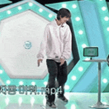 a man in a white shirt and black pants is standing on a stage in front of a computer monitor .
