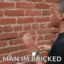 a man is standing in front of a brick wall talking to another man .