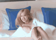 a woman is laying on a bed with blue pillows and a white blanket on her