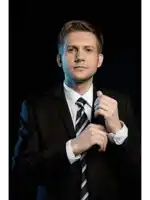 a man in a suit and tie looks at the camera with a black background