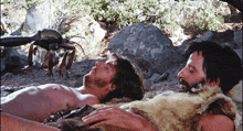 two men are laying on the ground with a crab behind them