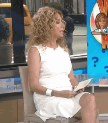 a woman in a white dress is sitting in a chair holding a piece of paper