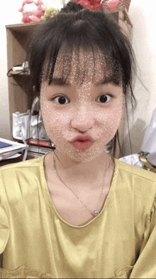 a girl wearing a yellow shirt and a necklace makes a funny face
