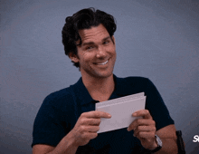 a man in a blue shirt is holding a piece of paper with the letter s on it
