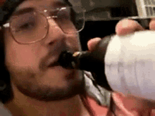 a man wearing glasses is drinking from a bottle of beer .