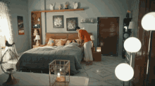 a woman standing next to a bed in a bedroom with lamps on the floor