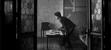a black and white photo of a man standing next to a table .