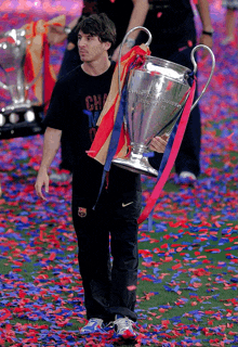 a man in a black shirt with the word champions on it holds a trophy