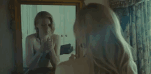 a woman is smoking a cigarette in front of a mirror while looking at herself .