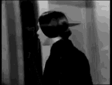 a black and white photo of a woman standing in front of a door in a room .