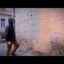 a man in a hooded jacket is walking along a brick wall