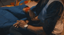 a man is standing next to a woman laying in bed with a blue blanket