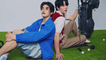 two men are sitting back to back on the grass with a golf bag and a golf club