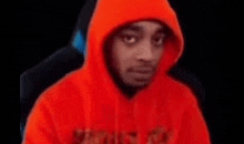 a man wearing a red hoodie is sitting in a chair and making a funny face .
