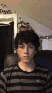 a young boy in a striped shirt is sitting in a chair and making a funny face .