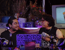 two men sitting at a table with a laptop that says carlock